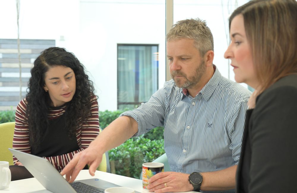 A senior C5 team leader demonstrates a new app they have developed on a laptop computer while the clients watch and review